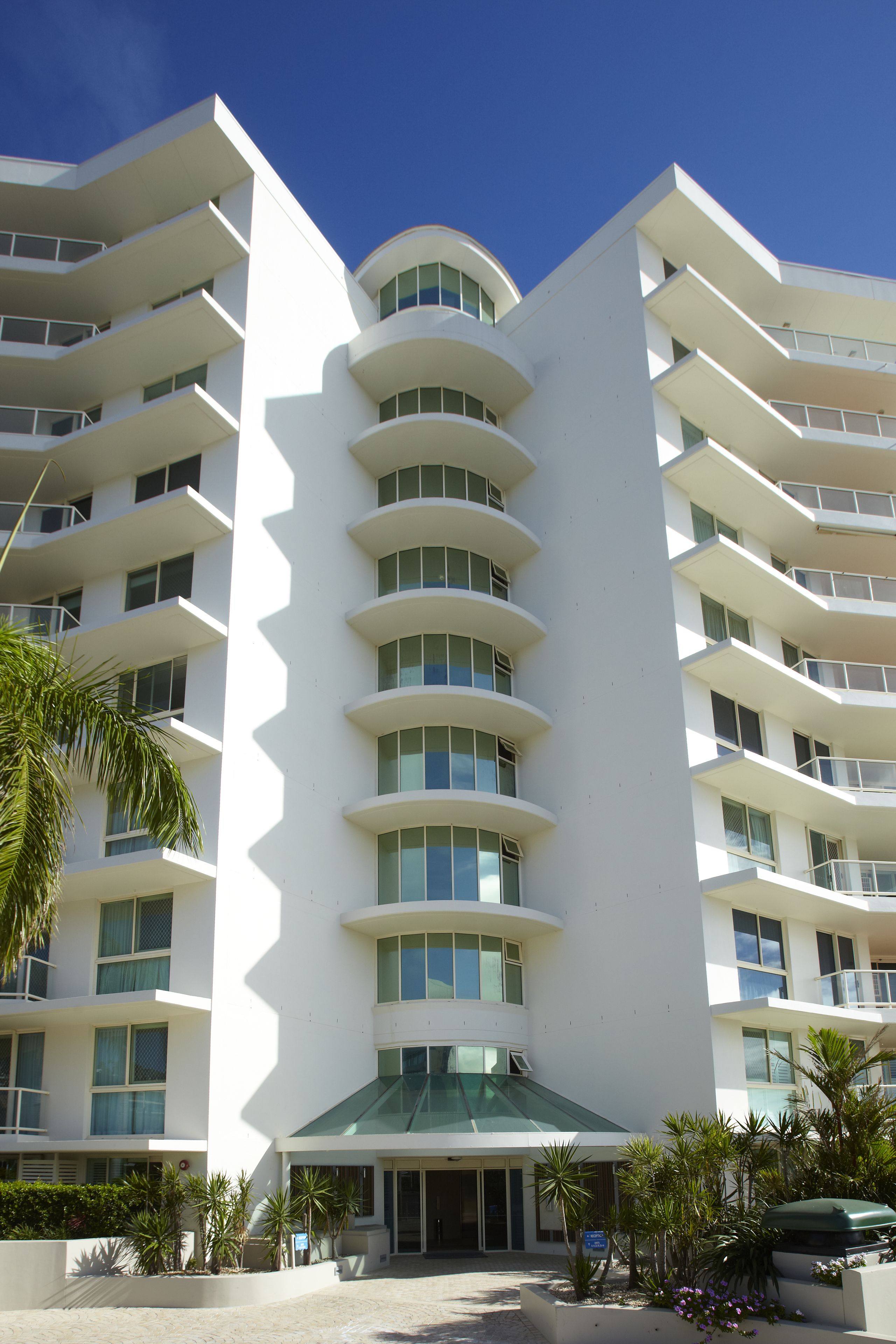 A multi-story hotel with a curved facade, balconies, and a covered entrance area.