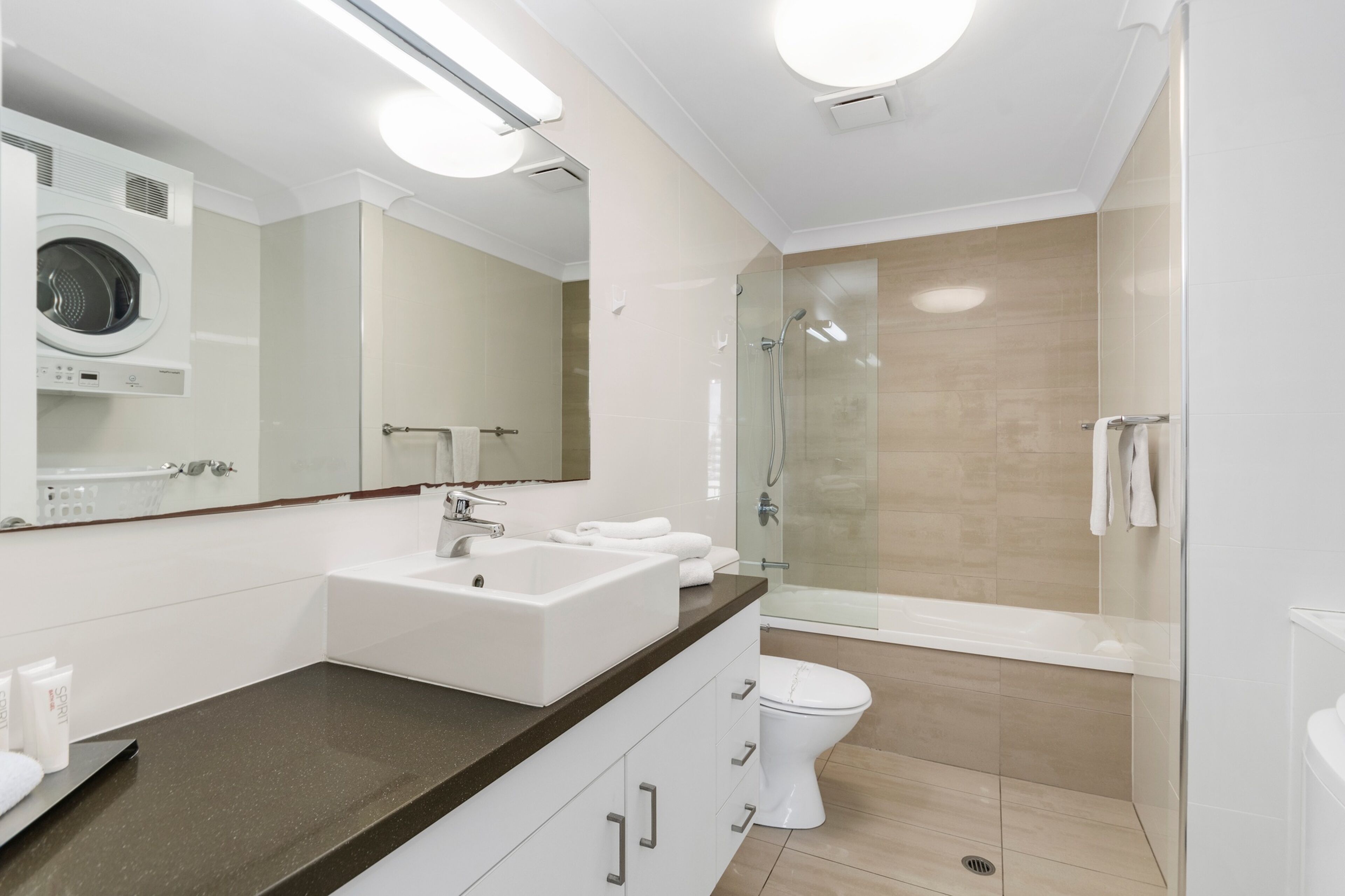 Une salle de bain moderne équipée d’un lave-linge intégré, d’une douche à parois de verre et de toilettes blanches.