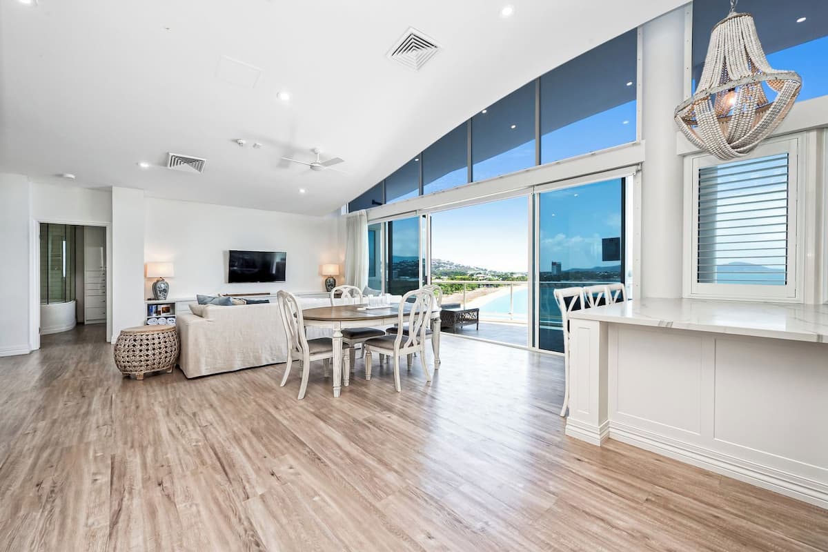 A modern living room with a dining area, large windows, and a view of the sea.