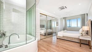 Una camera d'hotel moderna con vasca da bagno in vetro, un letto grande, un comodino e vista sulle montagne dalla finestra.