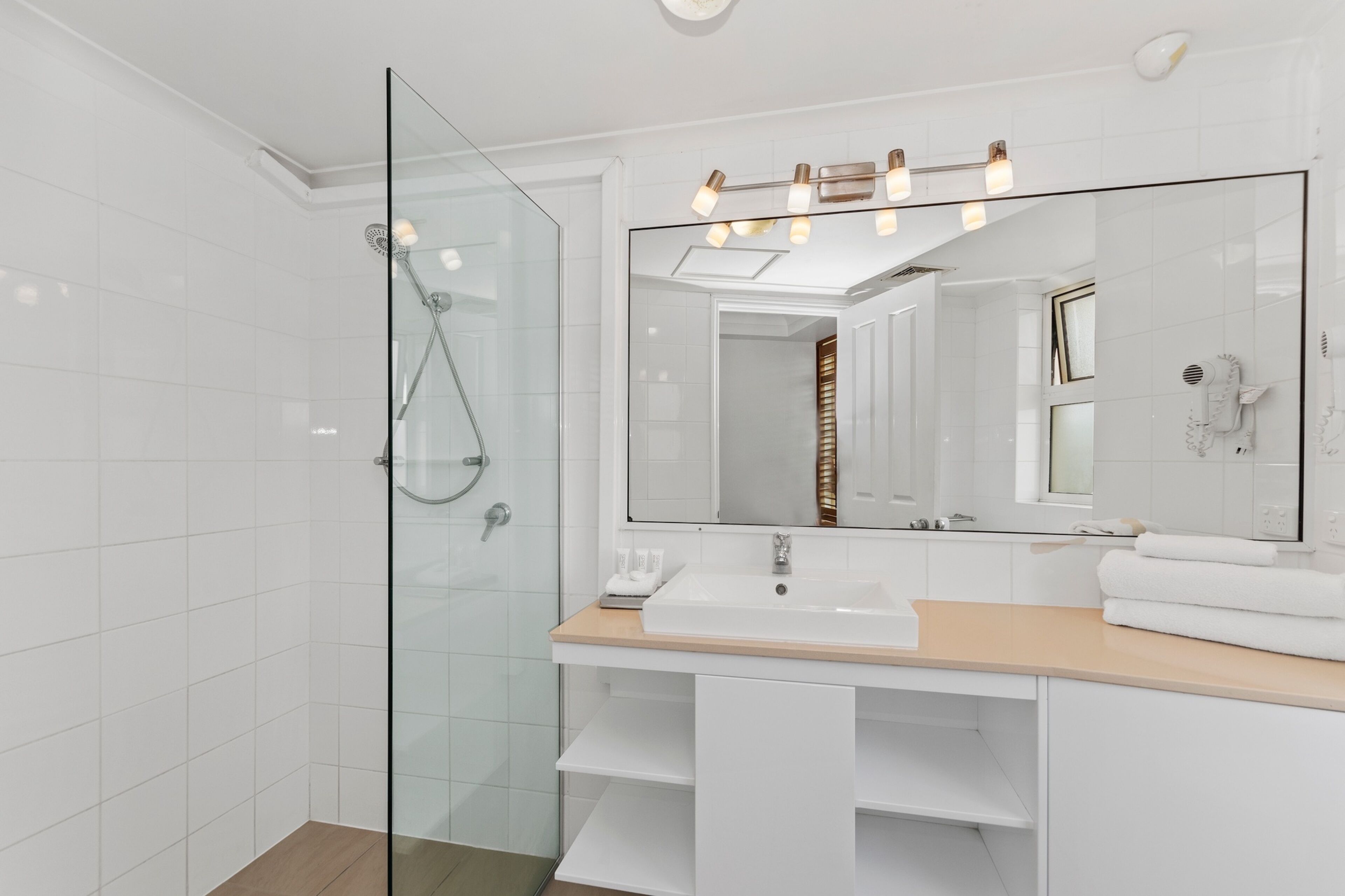 A modern bathroom with a glass-enclosed shower, a large mirror, and a white sink.