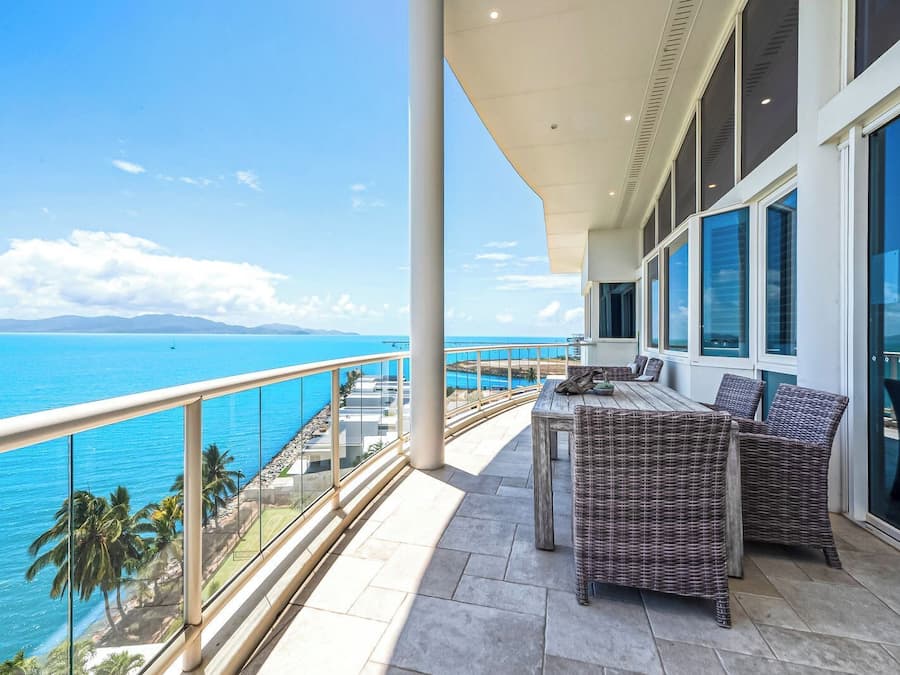 A balcony with wicker furniture, large windows, and a view of the ocean.