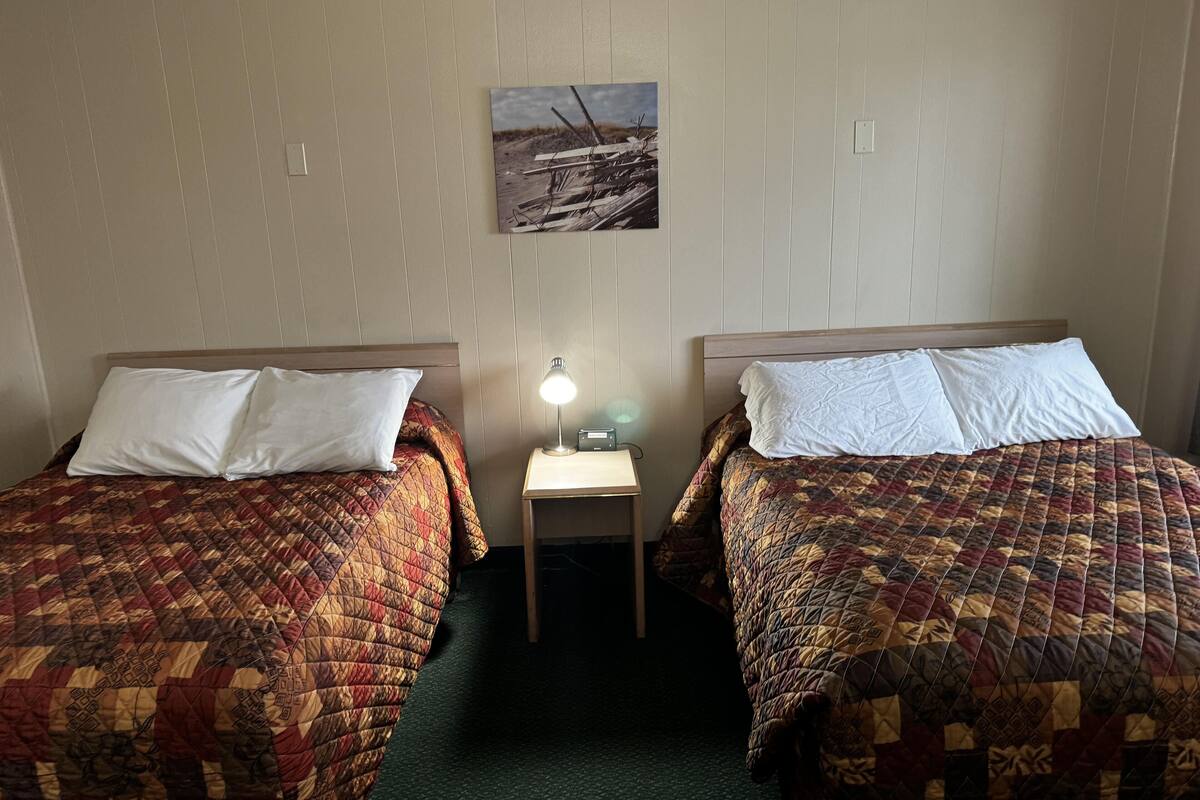 Une chambre d’hôtel avec deux lits, chacun recouvert d’une courtepointe à motifs, une petite table de chevet avec une lampe et un tableau accroché au mur.
