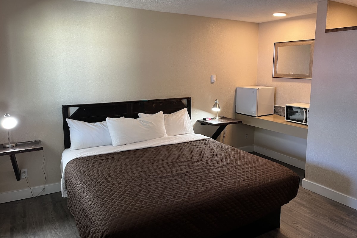 Une chambre d’hôtel avec un lit, une table de chevet, une lampe et un four à micro-ondes posé sur un comptoir.