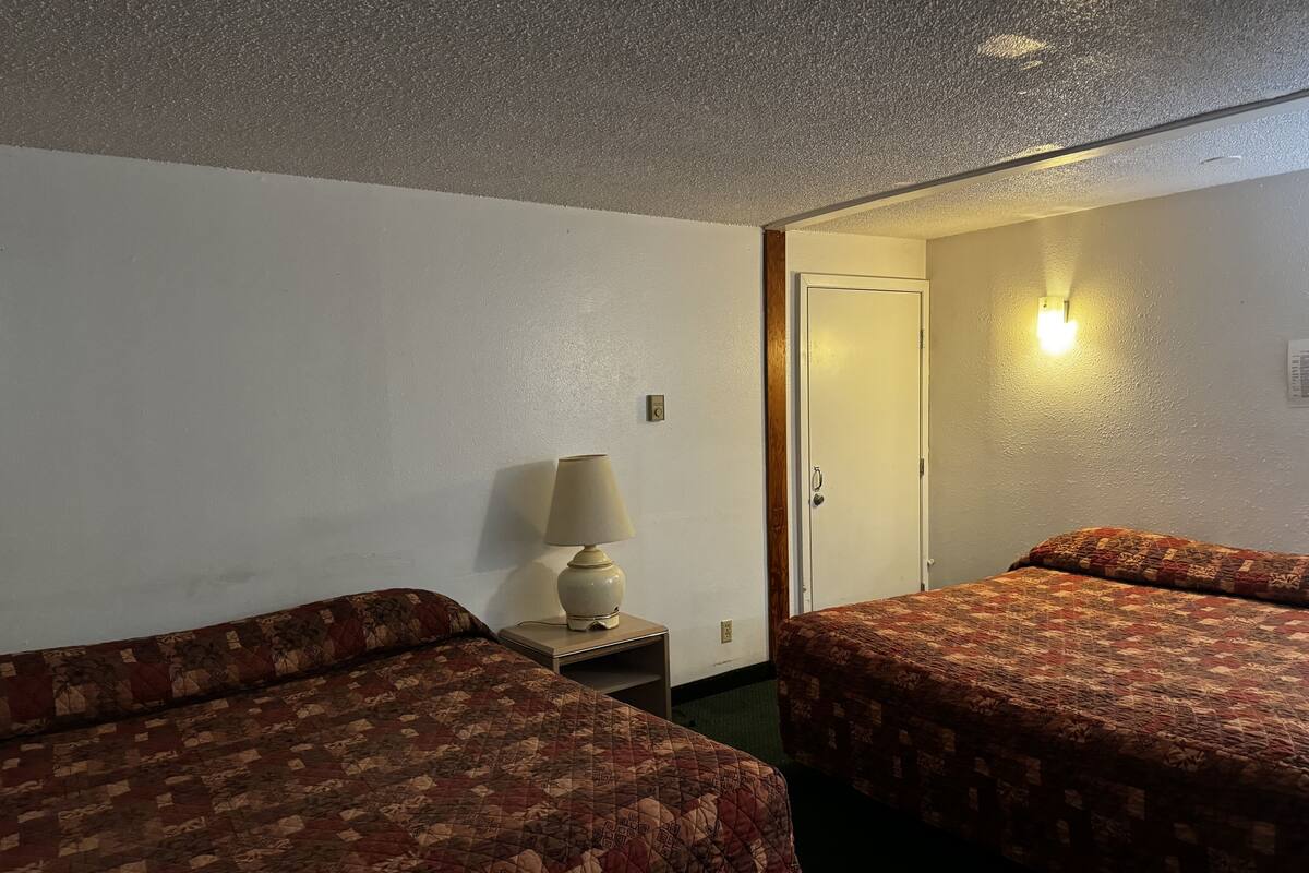 Une chambre d’hôtel avec deux lits, une table de chevet, une lampe et une porte donnant sur une autre pièce.