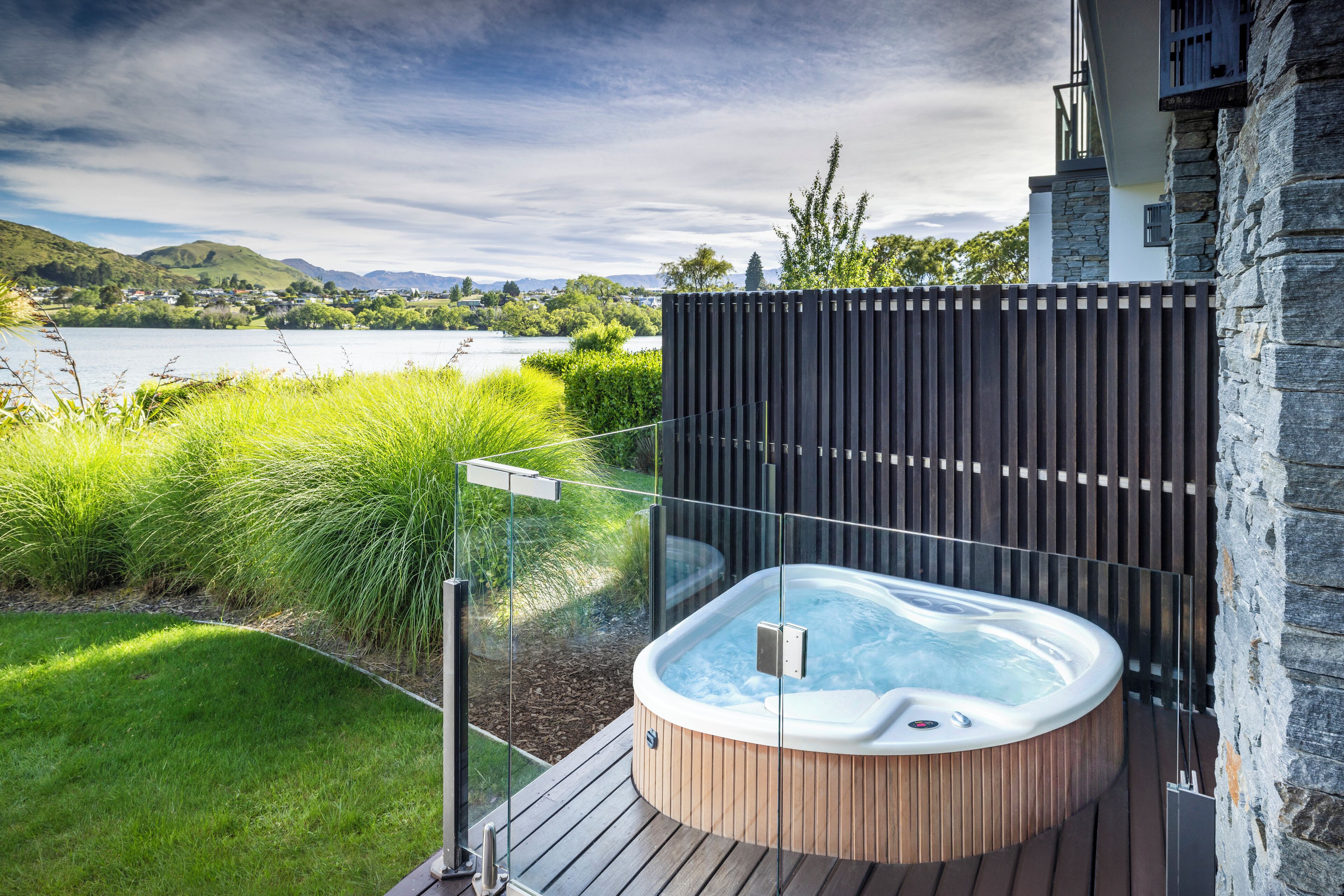A hot tub on a wooden deck with a view of a lake and hills.
