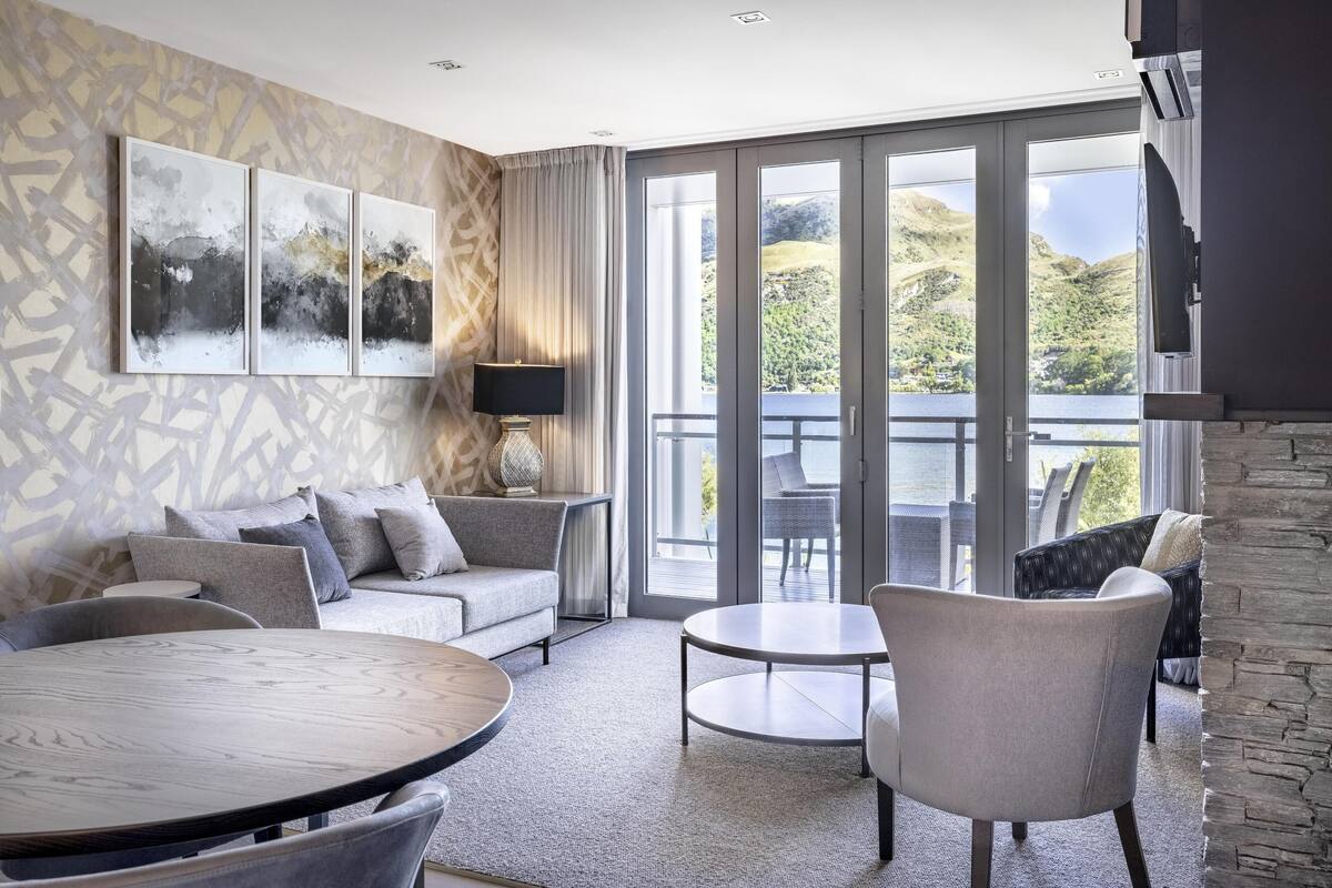 A modern living room with a large window, a sofa, a dining table, and a fireplace.