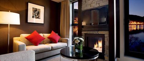A modern living room with a fireplace, a sofa, a coffee table, and a large window offering a view of a cityscape at dusk.