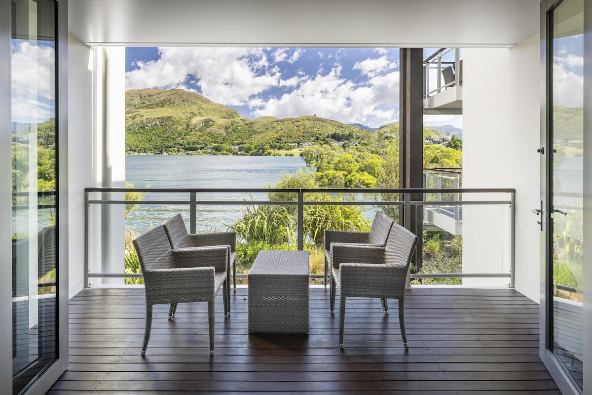 A balcony with wicker furniture and a view of a lake and hills.