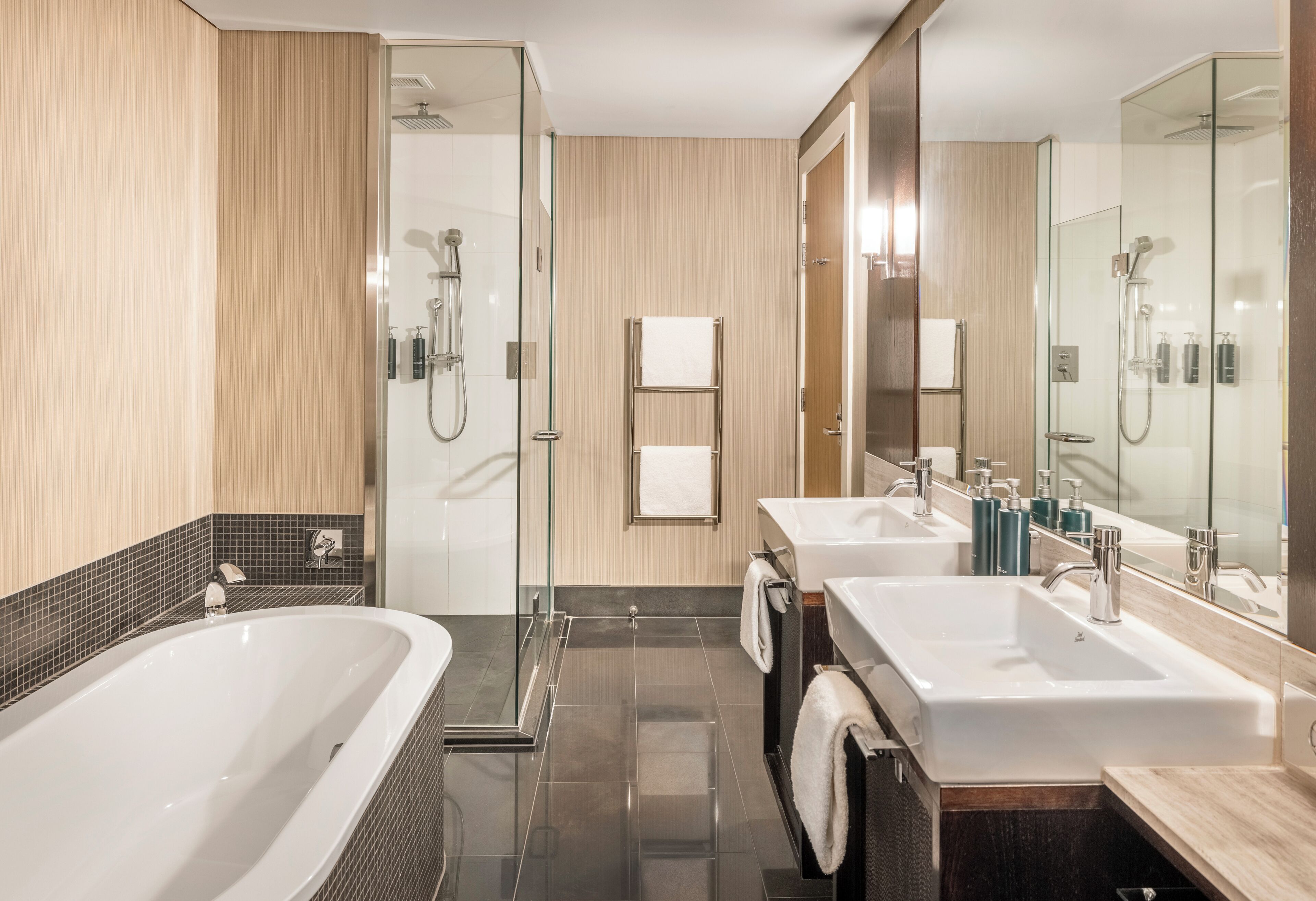 A modern bathroom with a glass-enclosed shower, two sinks, and a large bathtub.