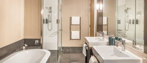A modern bathroom with a glass-enclosed shower, two sinks, and a large bathtub.