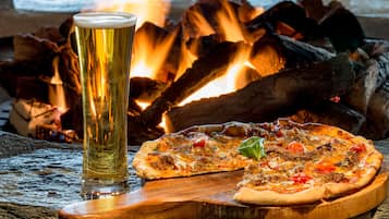 A pizza on a wooden board with a glass of beer in front of a fire.