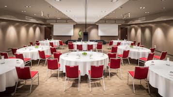 A conference room with multiple round tables, each with white tablecloths and red chairs, equipped with water bottles and nameplates.