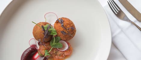 A plate of food with two round, golden-brown items, possibly croquettes, garnished with greens and radish slices, and a dark sauce.