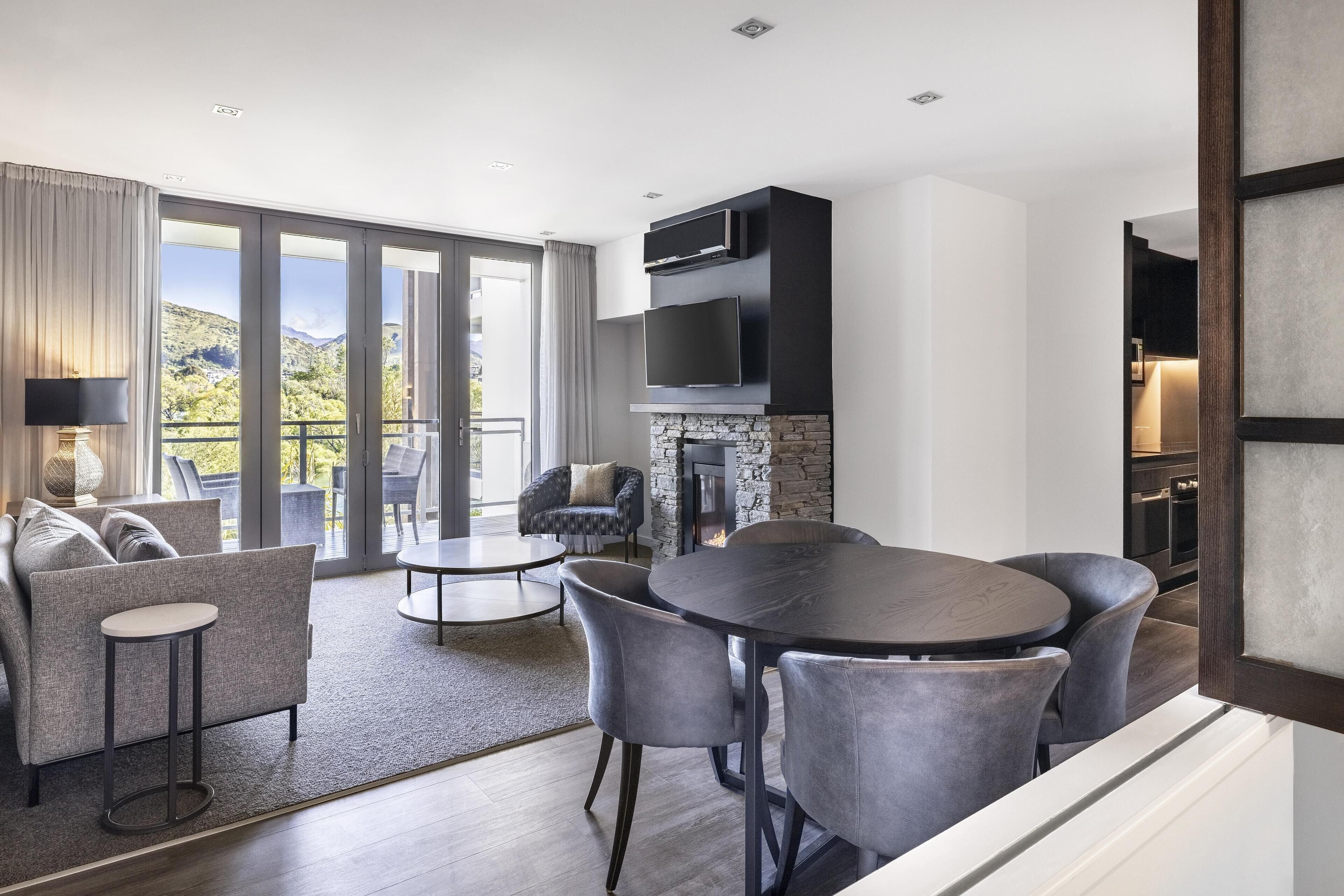 A modern living room with a fireplace, a dining area, and a balcony with a view of the mountains.