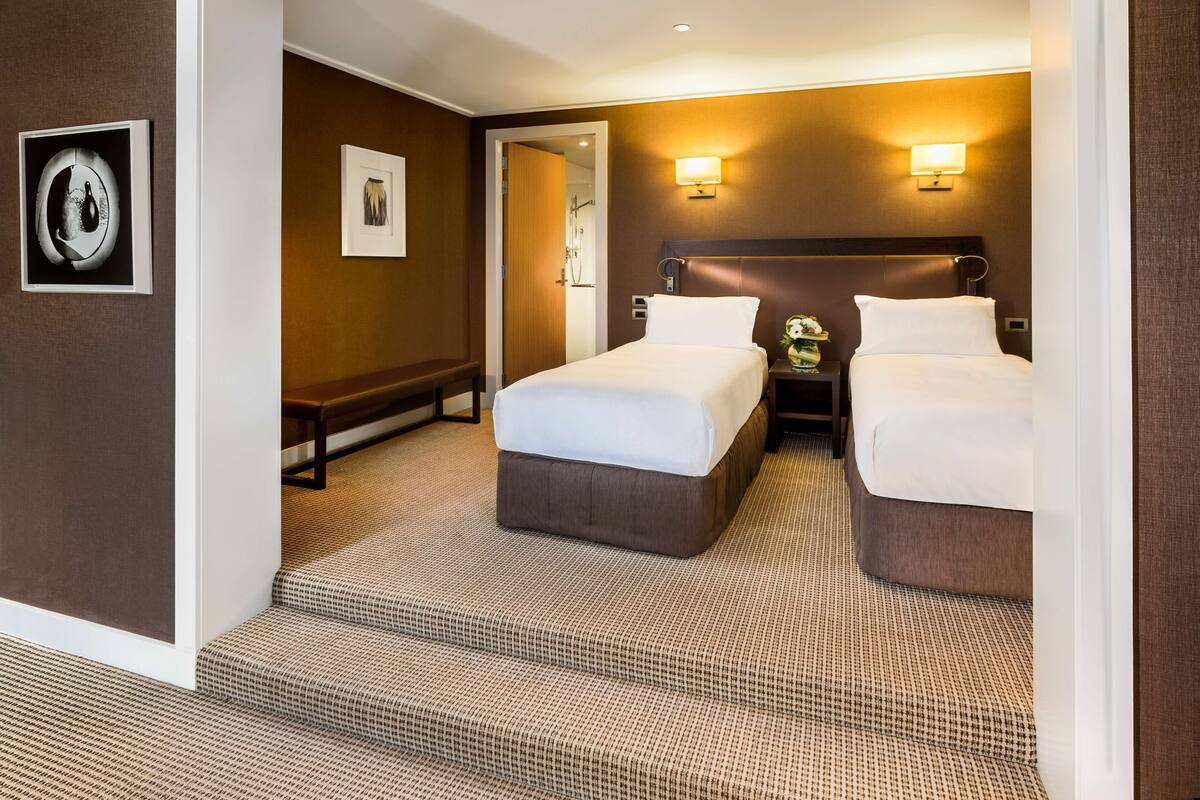A hotel room with two beds, a bathroom, and a hallway.