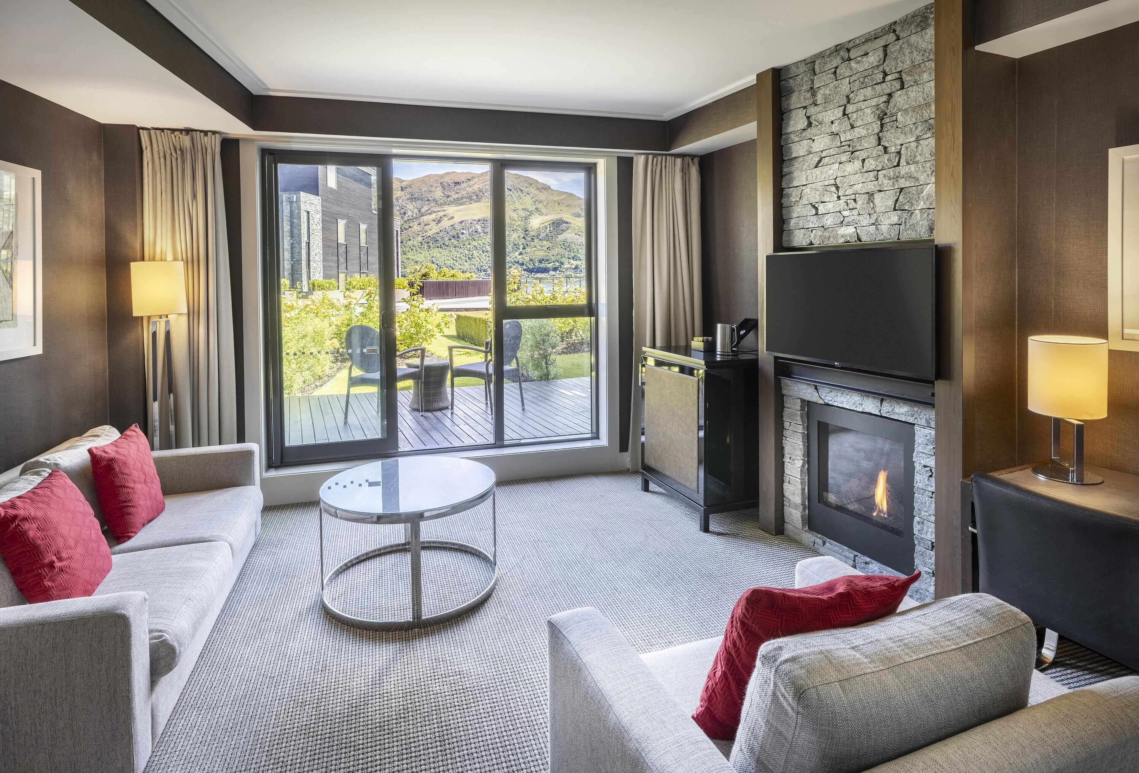 A modern living room with a fireplace, a sofa set, a round coffee table, and a large sliding glass door leading to an outdoor area.