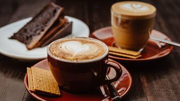 A cup of coffee with latte art on a saucer, a plate with a slice of cake, and a plate with a biscuit.