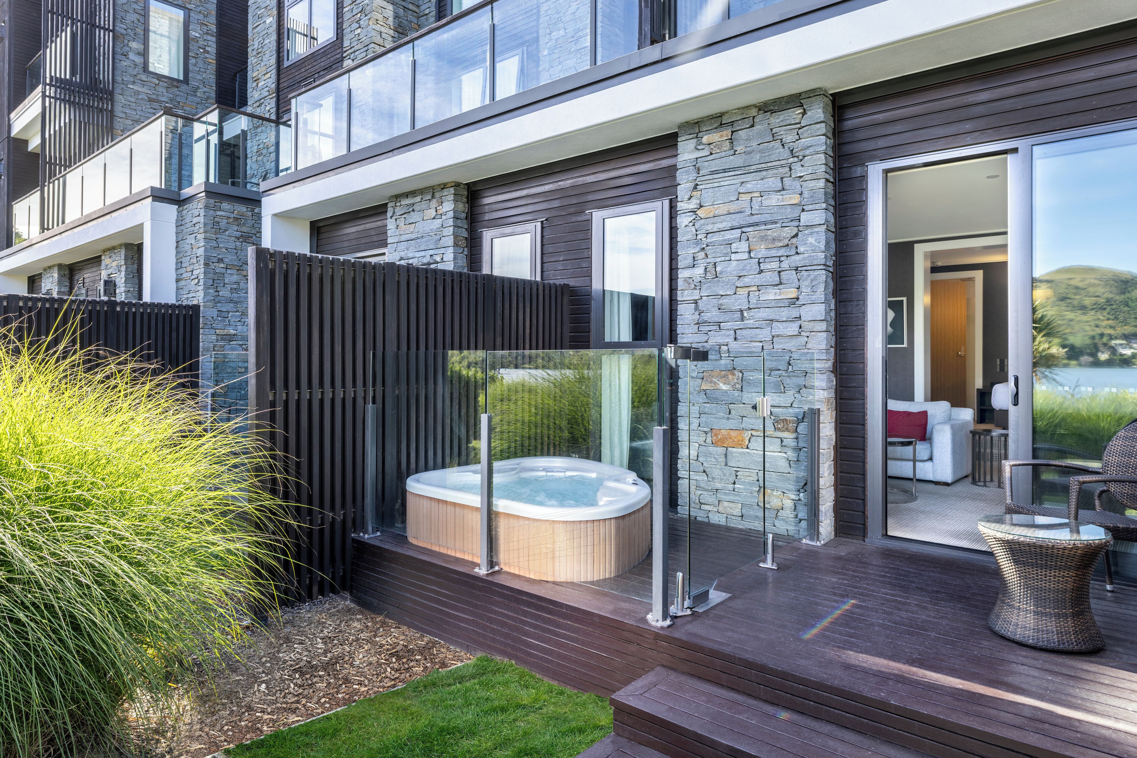 A modern house with a hot tub, outdoor seating, and a glass door leading to a living area.