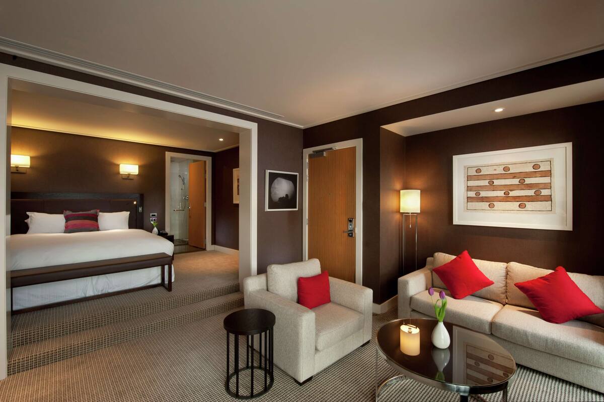 A hotel room with a large bed, a sofa, a coffee table, and a small side table.