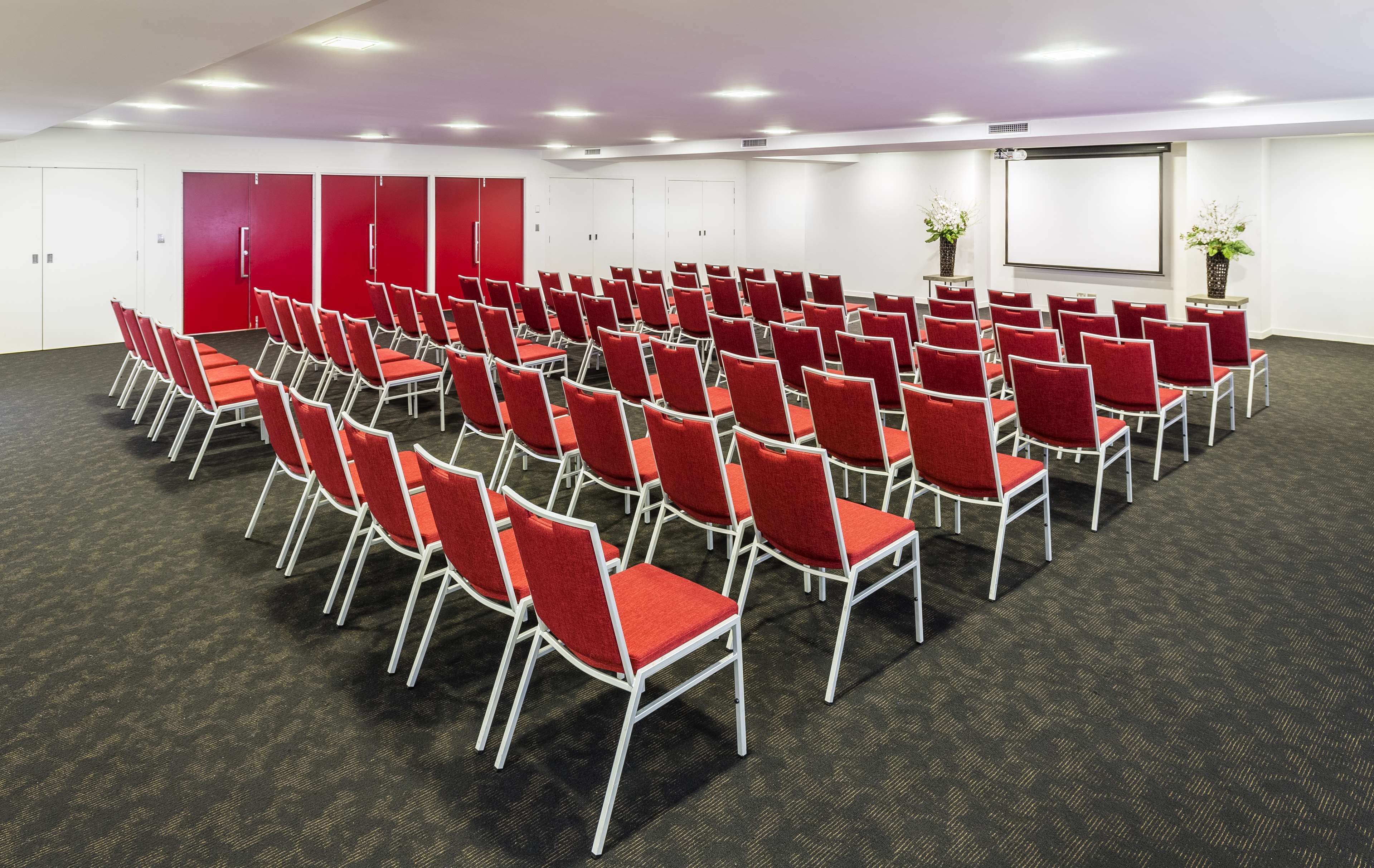 Ein Konferenzraum mit Reihen roter Stühle, einer Whiteboard und einer Projektionsleinwand.