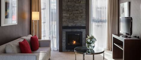 A modern living room with a stone fireplace, a sofa with red cushions, a glass coffee table, and a flat-screen TV on a wooden console.