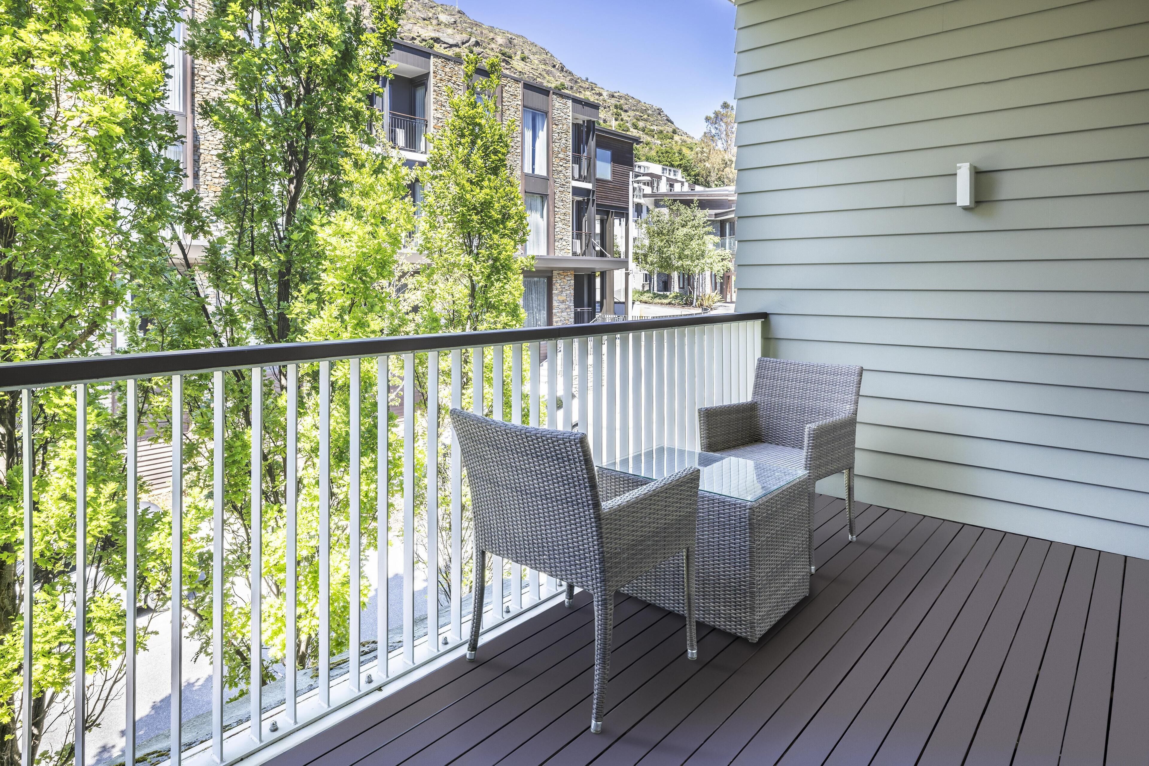A balcony with wicker furniture, a view of a tree-lined street, and a building with stone and wood elements.
