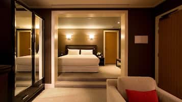 A hotel room with a large bed, a sitting area with a red pillow, and a mirror reflecting the room.