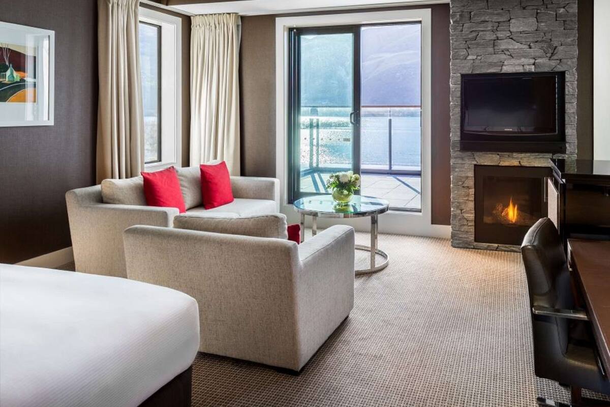 A modern hotel room with a sofa, armchair, and a flat-screen TV mounted on a stone wall.