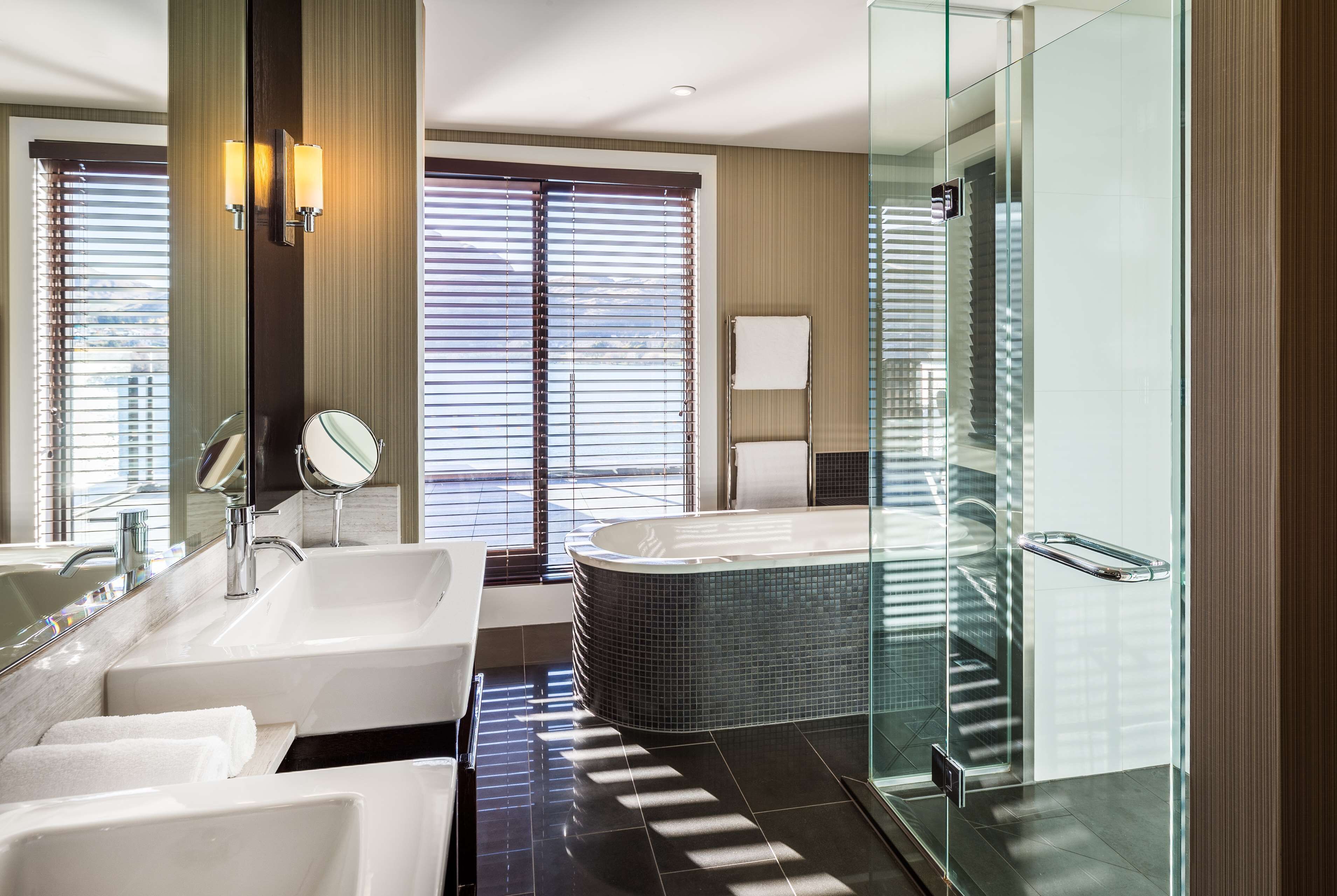 A modern bathroom with a large bathtub, two sinks, and a glass shower enclosure.