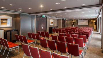 A conference room with rows of red chairs, a projector screen, and a podium.