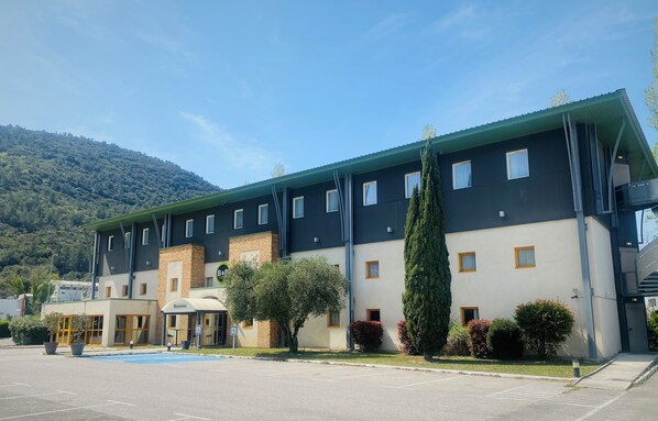 A multi-story hotel with a flat roof, a parking lot, and a mountainous backdrop.
