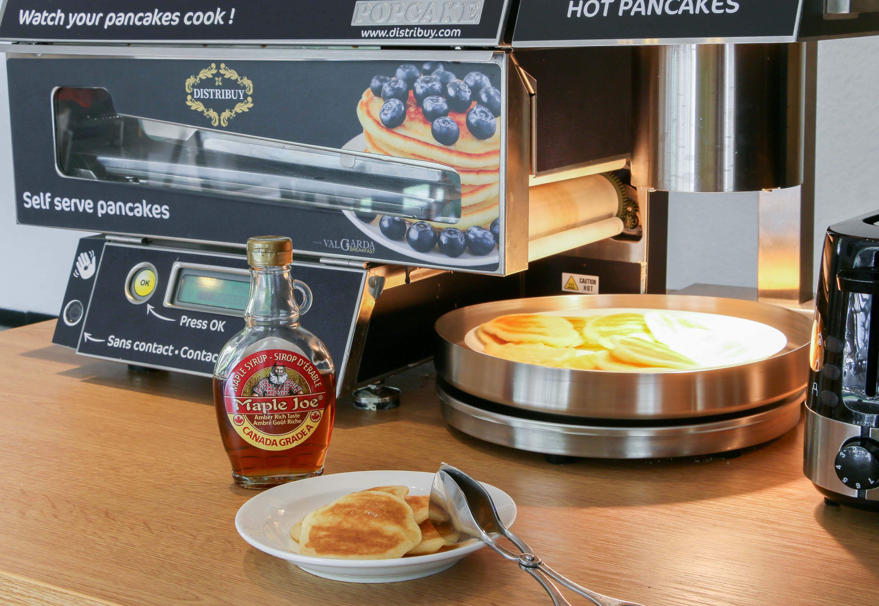 Une machine à crêpes en libre-service, accompagnée d’une bouteille de sirop d’érable et d’une assiette de crêpes.