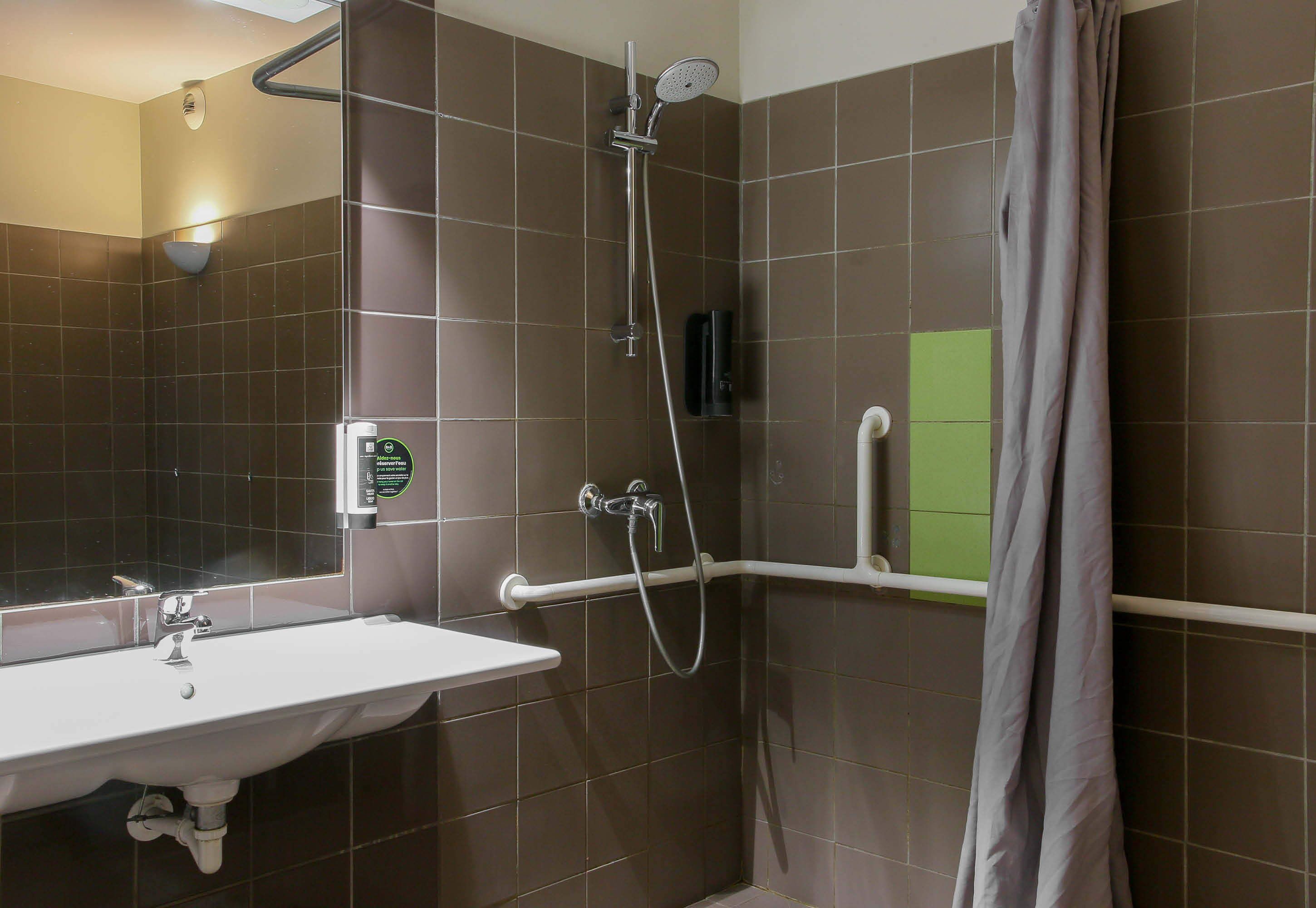 Un baño con lavamanos blanco, ducha con cabezal de ducha manual y toallero.