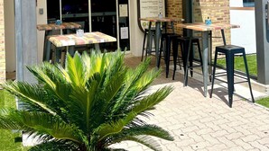 Entrada de un hotel B&B con un cartel que dice 'Bienvenue', asientos al aire libre y una planta de palmera en primer plano.