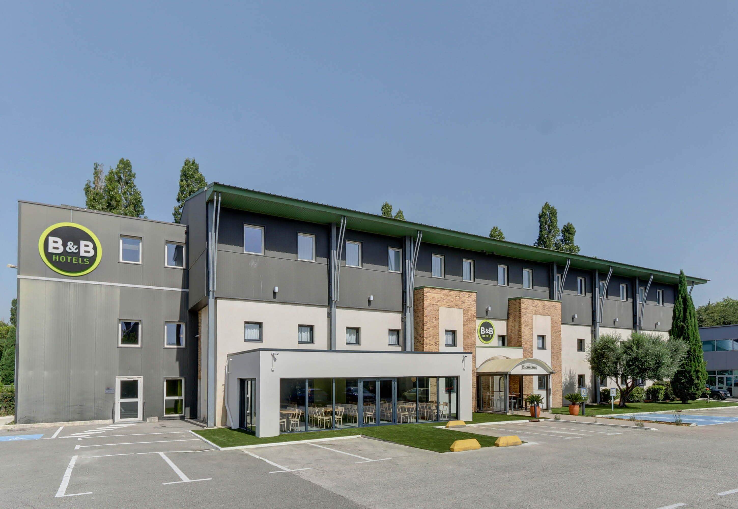 A B&B hotel with a modern design, featuring a large glass entrance and a parking lot.