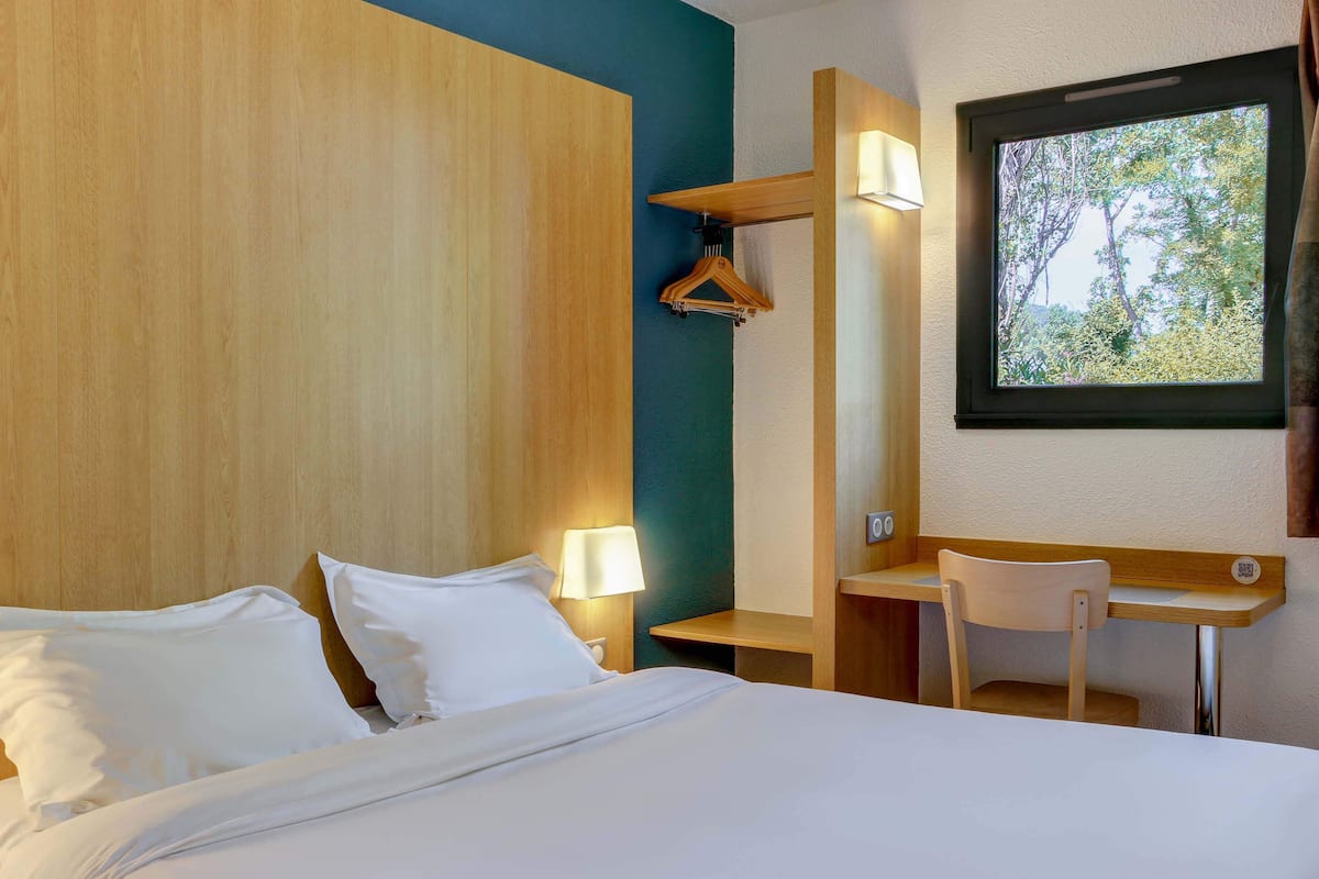 A hotel room with a bed, bedside lamps, a desk, and a chair.