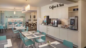 A modern café with tables and chairs, a coffee machine, and a sign that reads "Coffee & Tea". - Escala Hotel & Suites (Budapest)