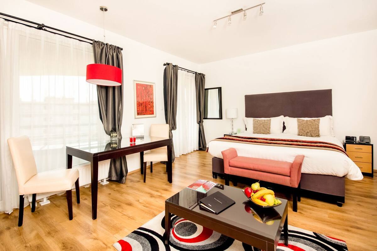 A hotel room with a bed, a desk, a chair, a dining table, and a coffee table.