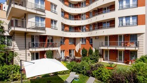 A multi-story apartment building with balconies, a garden area with sun loungers, and a white umbrella. - Escala Hotel & Suites (Budapest)