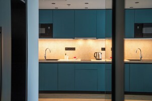 Cocina moderna con armarios azul verdoso, un lavamanos de acero inoxidable y un microondas.