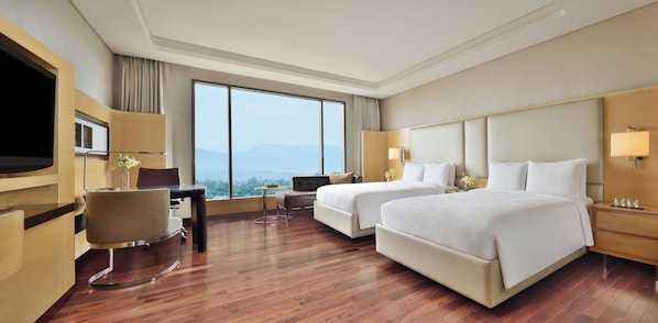 A hotel room with two beds, a desk, a chair, a TV, and a large window with a mountain view. - JW Marriott Hotel Chandigarh (Chandigarh)