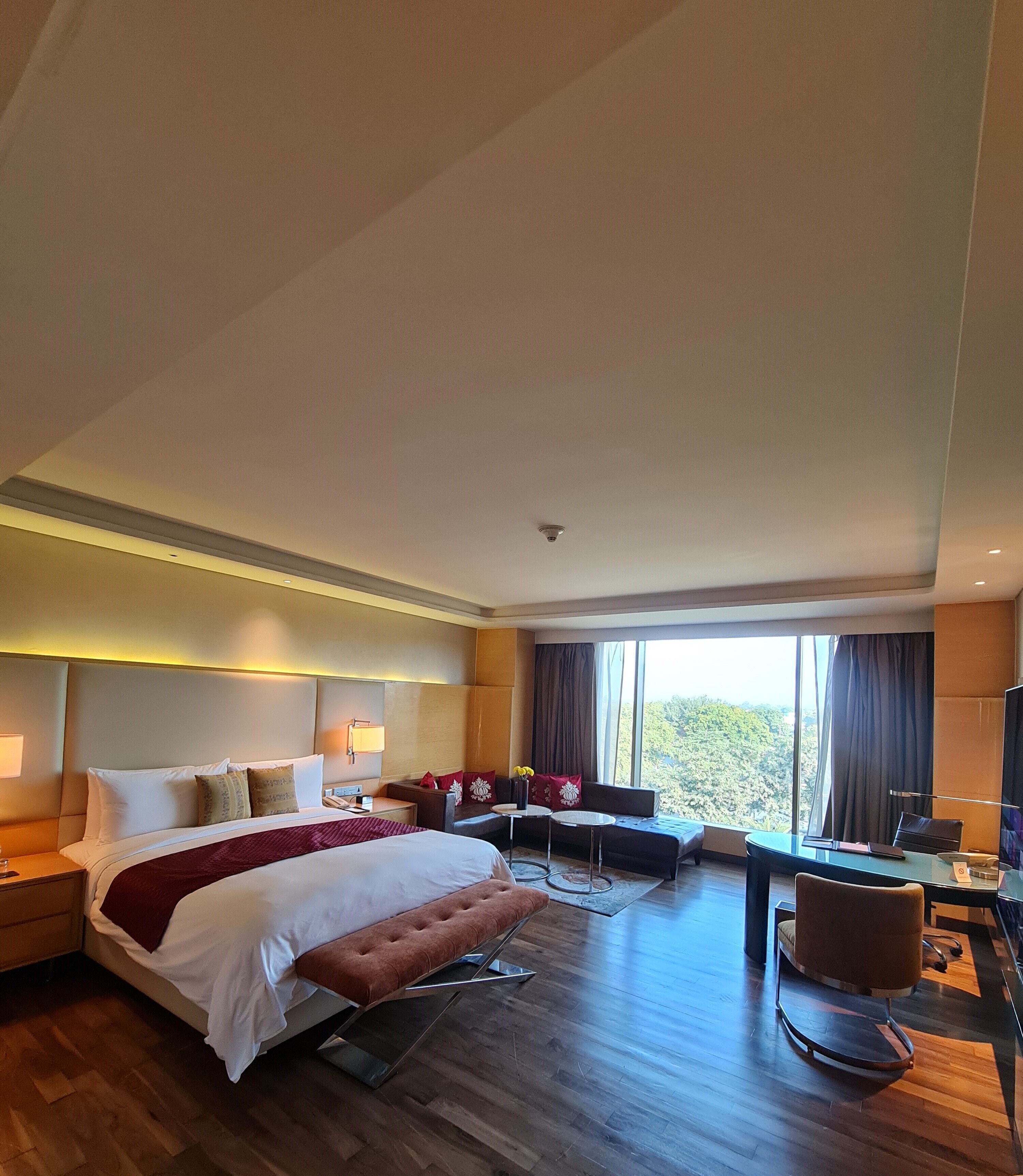 A hotel room with a large bed, a desk with a chair, a small round table, and a sofa.