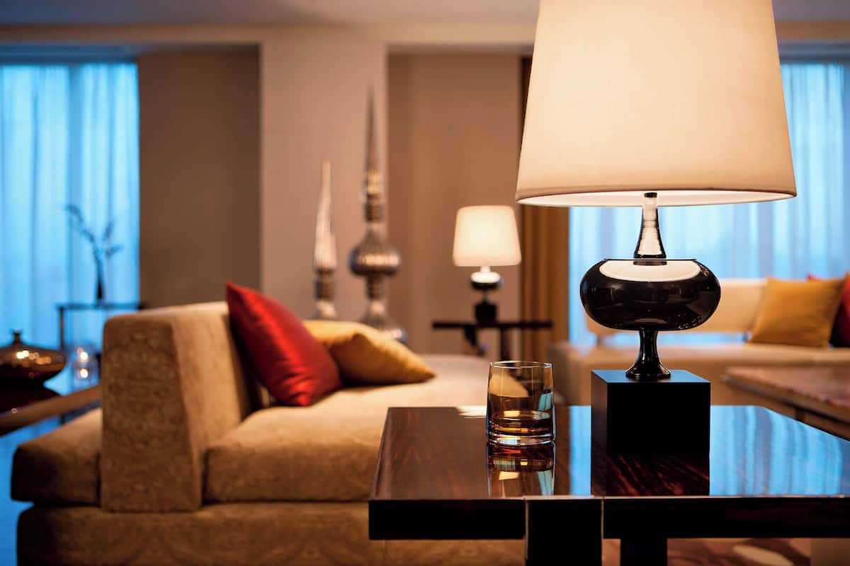 A well-lit hotel room with a sofa, a table with a glass of water, and a lamp.