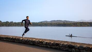 A man running along a stone wall beside a calm lake with a distant boat and hills in the background.