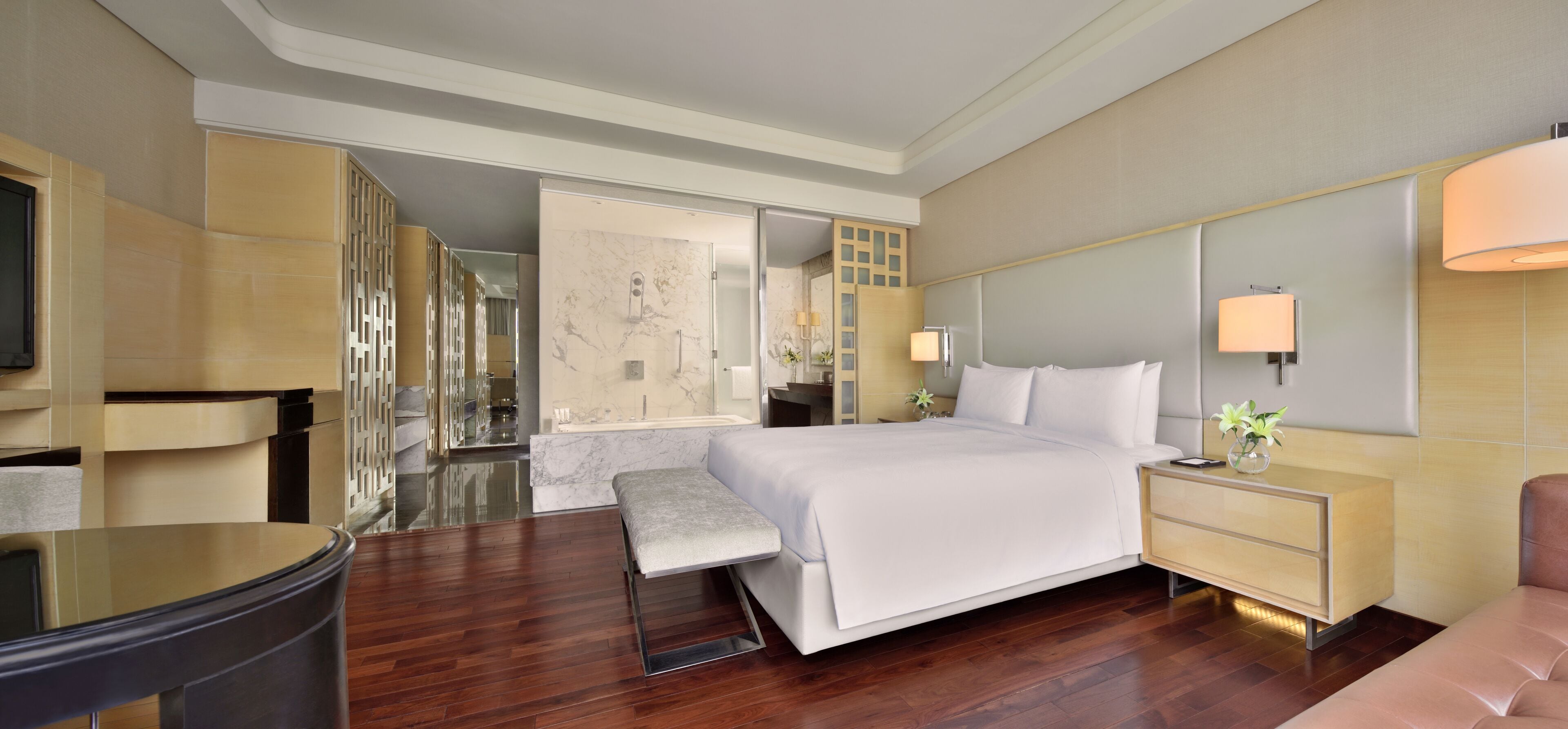 A modern hotel room with a large bed, bedside tables, a seating area, and a TV.