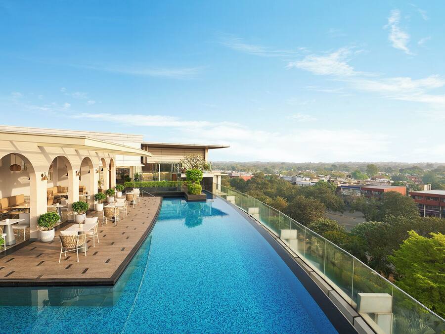 Una piscina infinita en la azotea con barandilla de cristal, mobiliario exterior y vistas a la ciudad.