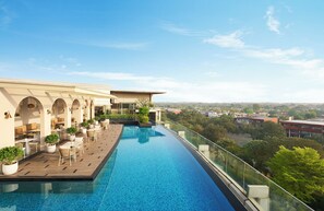 Una piscina infinita en la azotea con barandilla de cristal, mobiliario exterior y vistas a la ciudad.