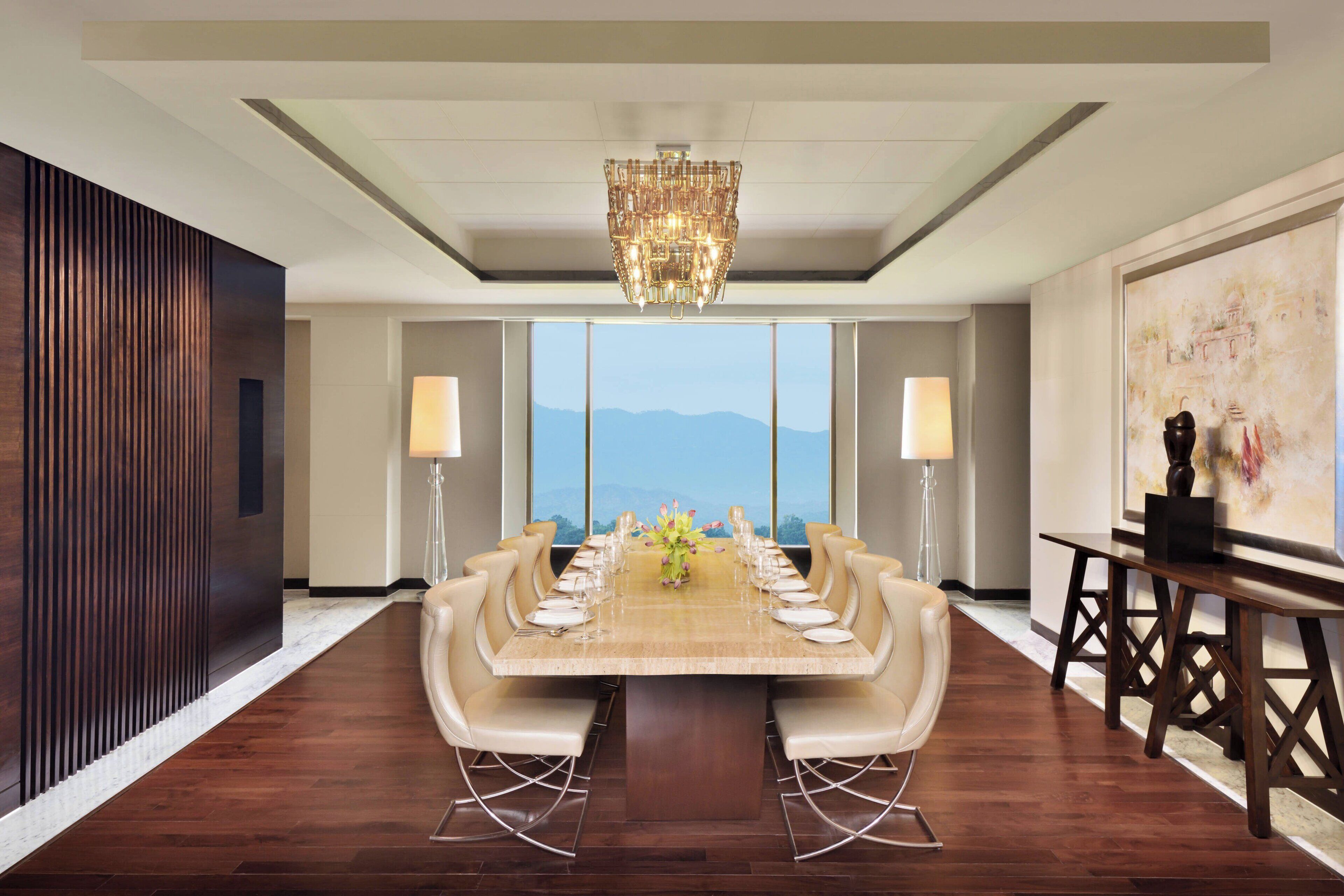Comedor formal con una larga mesa dispuesta para una comida, ventanas amplias con vista a las montañas y una araña.