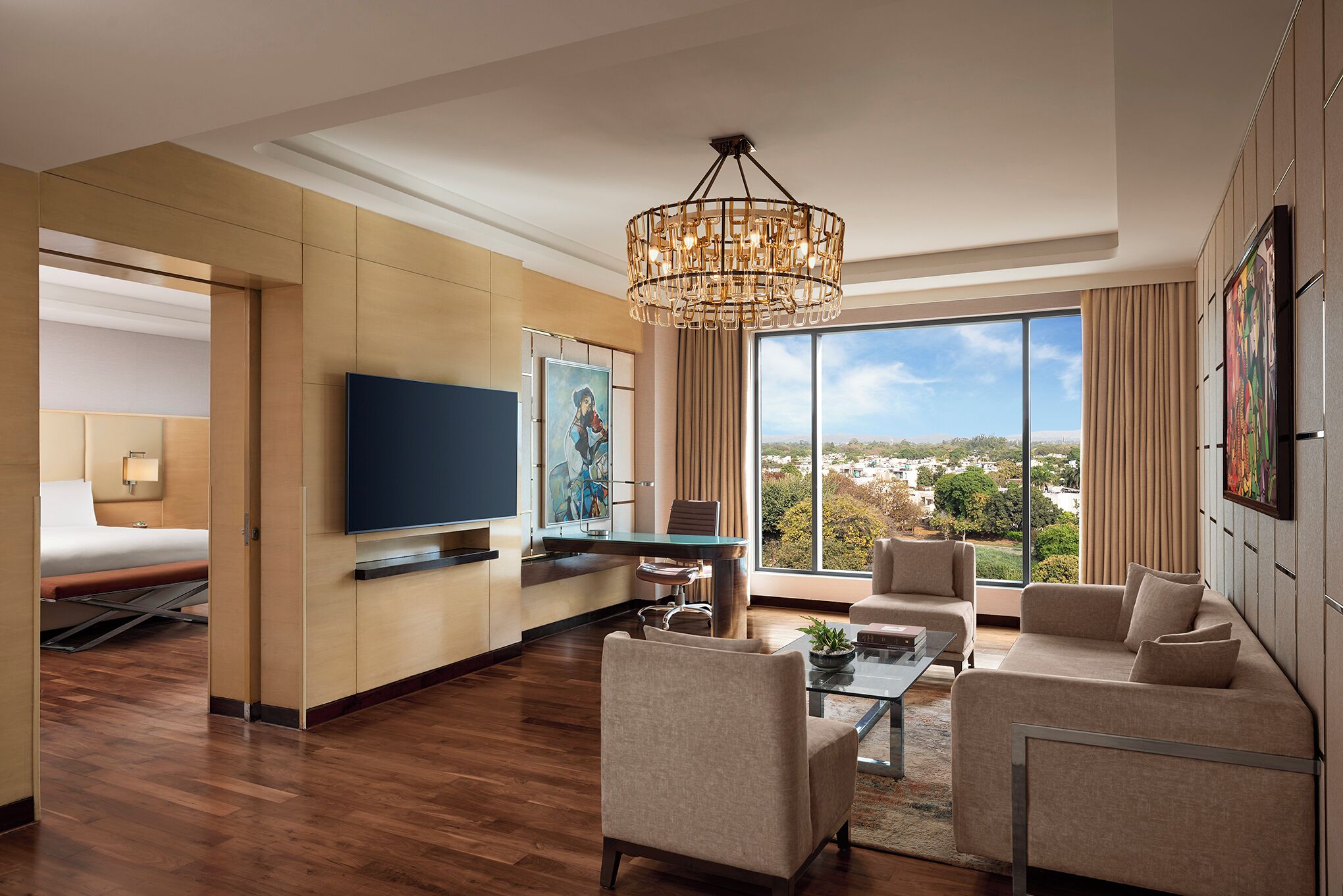 Una habitación de hotel moderna con una televisión de pantalla plana, zona de comedor, sofá y un amplio ventanal con vistas a la ciudad.